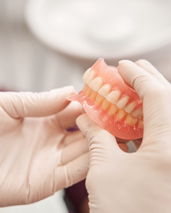 White-gloved hands holding a complete set of dentures