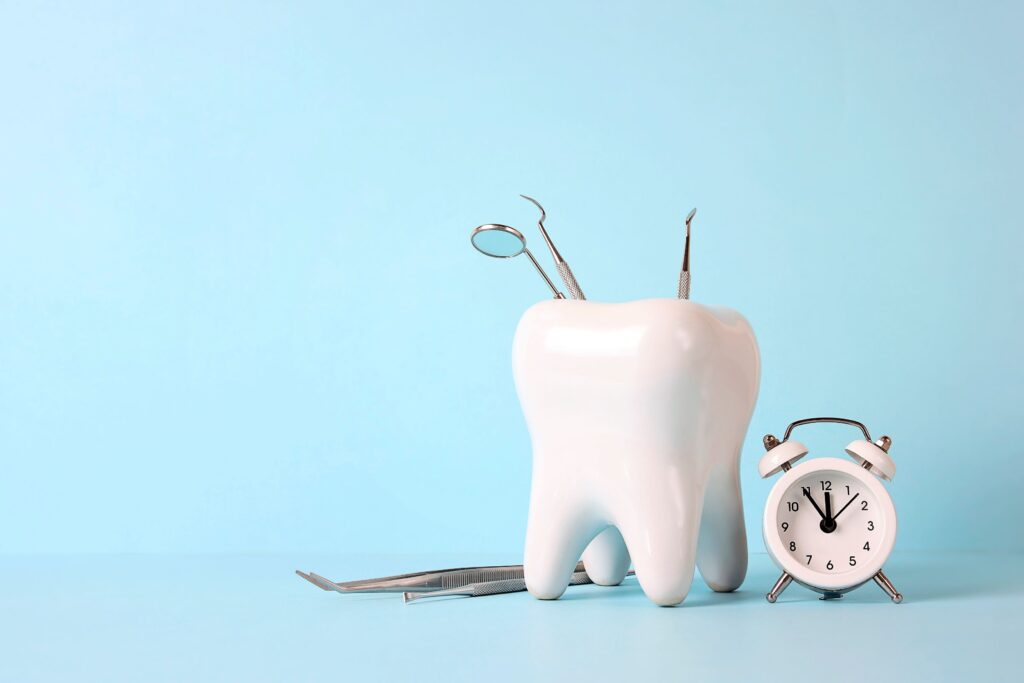 Dental instruments in a large model tooth next to a small white alarm clock with light blue background